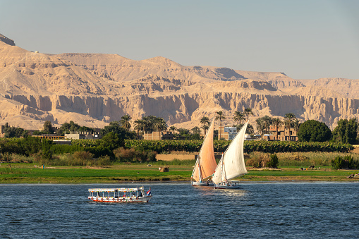 Traditional egyptian feluccas sailing boats on the Nile river, Theban mountains in the background in Luxor, Egypt