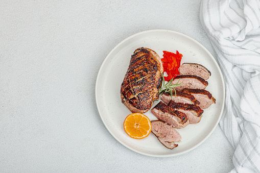 Fried duck breast with fresh orange and ginger, ready to eat food. Domestic tasty cuisine, poultry meat fillet. Light stone concrete background, top view