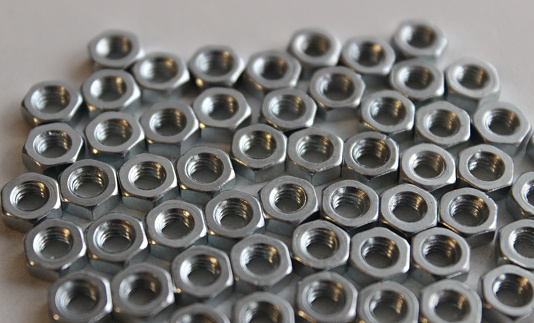 Hex nuts on a flat surface are huddled together on white surface