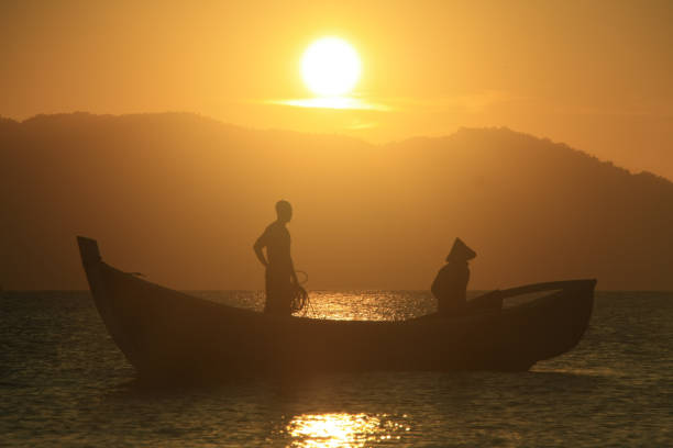silhouette of a fisherman working to clean his net of fish and rubbish at sunset on Kapung Java beach, Banda Aceh.02/14/2019