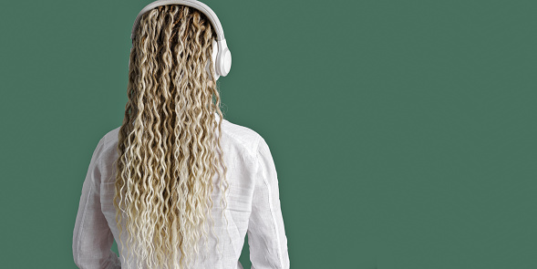 Carefree woman wearing white shirt in headphones on head, listening to music, female with blonde long hair, back view, time for yourself, rest, relaxation concept, no face or anonymity, wide banner