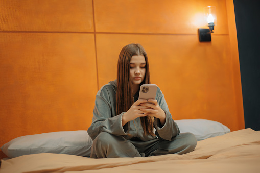 Girl sitting on the bed cross-legged watching a video on her phone