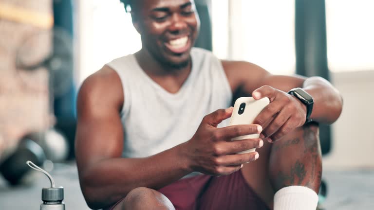 Happy, fitness and black man with phone in gym for social media, text message and online chat after workout. Sports, typing and person on smartphone or mobile app for training, exercise and wellness