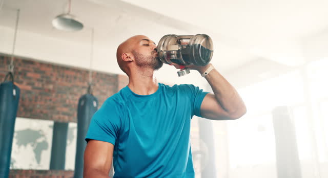 Man, fitness and drinking water on break at gym for hydration, recovery or natural sustainability in workout. Thirsty or tired male person in rest, exercise or breathing with mineral liquid or bottle