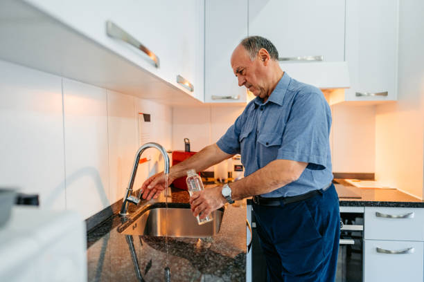 istock Senior Man Refiling His Glass Water Bottle With Water 2012890294