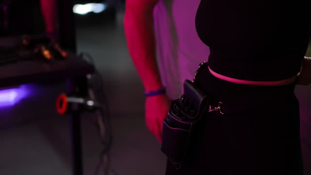 Close-up. An unrecognizable man helps an unrecognizable woman put a leather hairdressing tool bag on her belt. Slow motion.