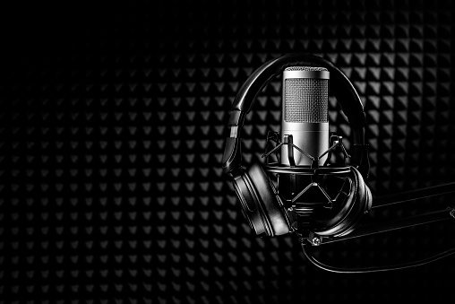 Studio condenser microphone with professional headphones and black acoustic sound proof panel.