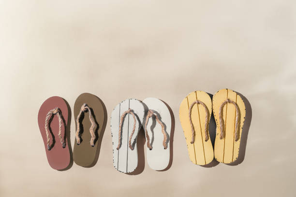 女性の夏の靴、サンダル、ハードシャドウ、ベージュのグラデーションカラーの背景にベージュの茶色の白いビーチサンダルと創造的なレイアウト。審美的なトレンド夏のファッションコン�