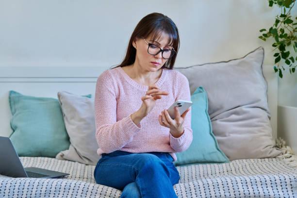 istock Middle aged woman using smartphone while sitting on couch at home 2012901650