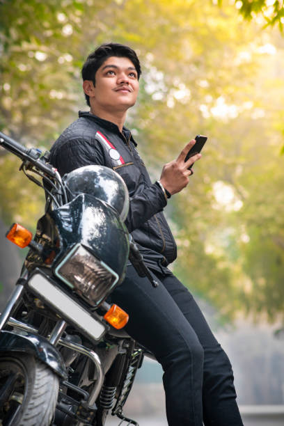 istock Handsome biker sitting on a motorcycle contemplating with holding smartphone in hand. 2012906570