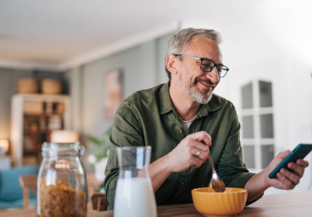 Happy senior man reading online newspaper while having breakfast