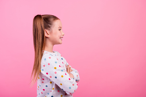 Side profile photo of cute small girl wear stylish sweatshirt arms crossed look at promo empty space isolated on pink color background.