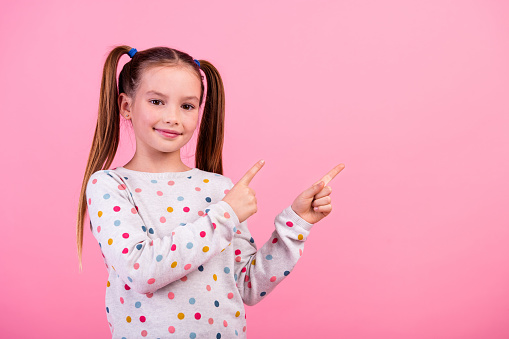 Photo of positive small girl with tails wear stylish sweatshirt directing at proposition empty space isolated on pink color background.