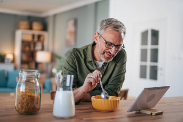 istock Happy senior man eating cereal for breakfast and using digital tablet 2012926997