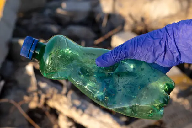Volunteer hand with blue glove holding plastic green bottle garbage. Close-up. Environmental activist clean and collect trash in nature. Ecology concept.