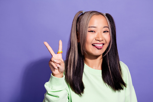 Portrait of funky youngster japanese girl wear green jumper tongue out posing k pop model shows v sign isolated on violet color background.