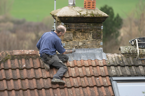 Leeds, UK - February 15, 2024: A man repairing a house roof and chimney in the UK.