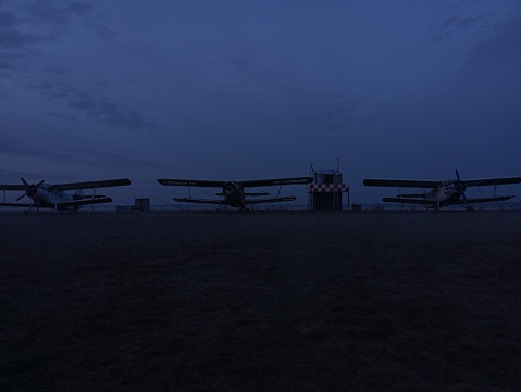 Three single-engine sport airplanes on the ground in the evening against a dark sky as the sun sets over the horizon. Aviation transport on the background of the sky.