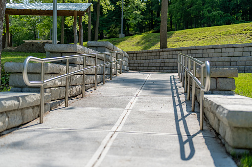 Outdoor, exterior gray concrete ramped sidewalk with stainless steel railings.