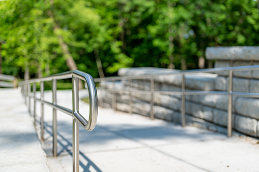 Outdoor, exterior gray concrete ramped sidewalk with stainless steel railings.