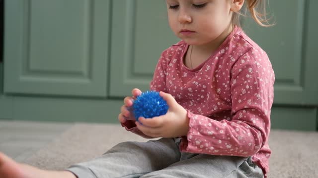 Cute baby girl playing tactile knobby balls. Young child hand plays sensory massage ball. Enhance the cognitive, physical process. Brain development. Support for Children with ADHD, autism, fidgeting.