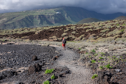 Rear view of an elderly man walking in the nature of Malpais de Guimar at Tenerife island with backpack on his shoulder
