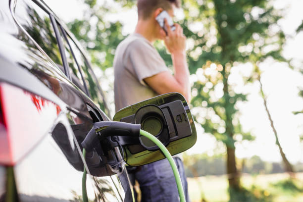 istock Young man charging electric car talking on smartphone 2013078693