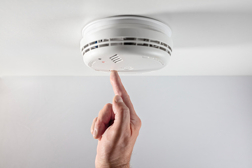 Home smoke and fire alarm detector maintenance man pushing button checking, testing or replacing battery