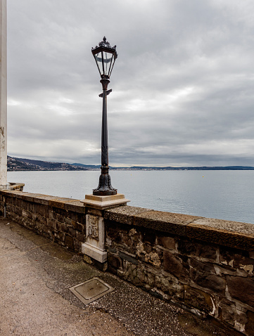 Trieste, Italy - February 12, 2024: Waterfront near the Miramare Castle, with street lamp and overlook on the gulf.