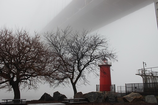 Panoramic view of the Little Red Lighthouse with its flashing light on by the Hudson River under the George Washington Bridge on a foggy winter day in Riverside Park, Washington Heights