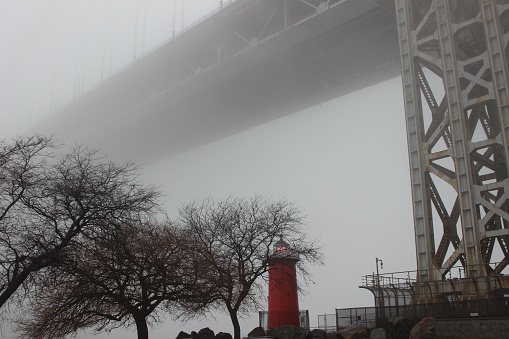 Panoramic view of the Little Red Lighthouse with its flashing light on by the Hudson River under the George Washington Bridge on a foggy winter day in Riverside Park, Washington Heights