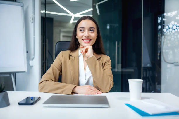 istock Attractive businesswoman looking aside while sitting at work desk with laptop in office. Confident pretty caucasian lady dreaming of opportunities indoors 2013109325