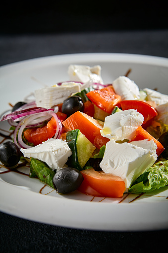 Greek salad closeup with feta cheese, Kalamata olives, and balsamic glaze on a white plate.