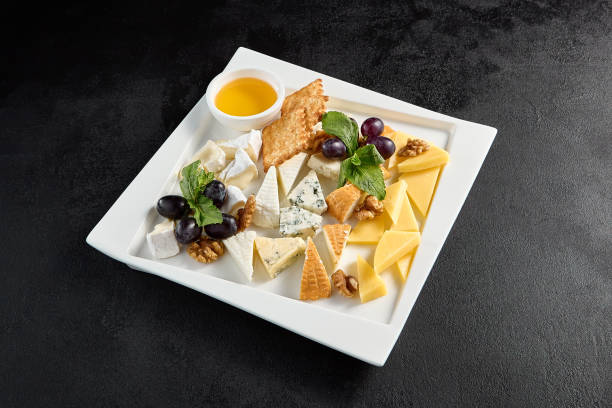 istock Cheese board with grapes and honey on a white plate against a black background 2013145754