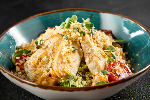 Quinoa salad with grilled chicken, cherry tomatoes, and greens in a turquoise ceramic bowl.