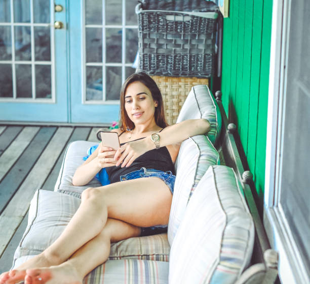 istock Beautiful young woman relaxes on sofa in summer clothes using cell phone 2013165482