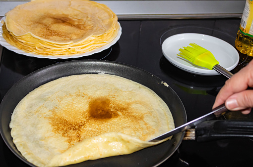 Woman hand frying homemade crepes in a pan on the  stove