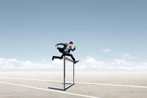 A businessman jumps over a hurdle on his way to his destination.