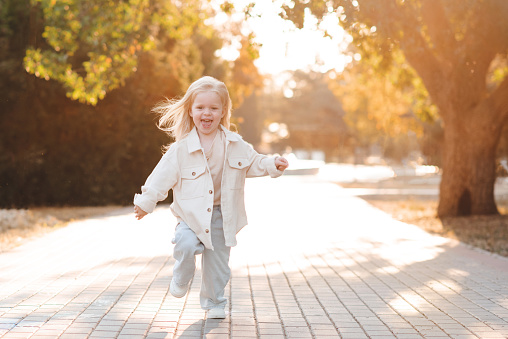 Smiling child girl 2-3 year old wearing stylish clothes running and having fun in park over sun light outdoor. Childhood. Spring season.