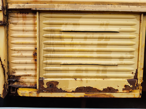Close-up on yellow side panels of a vintage car with lots of rust and stains.