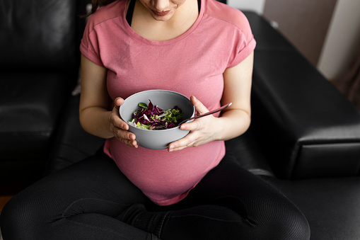 Smiling pregnant woman eating healthy salad at home