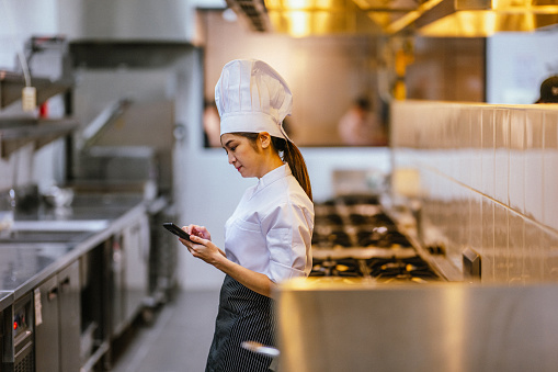 Portrait of an Asian Chinese female student using a smartphone during  in commercial kitchen at cooking school.