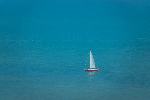 Sailboat sails gracefully across turquoise blue off the coast of South England. Favorable sailing conditions and a beautiful sunny summer day to explore the picturesque English coastline from a boat.