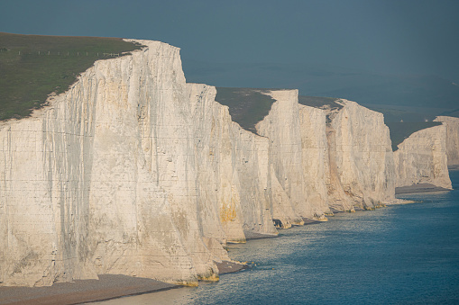 Incredible grandeur of white cliffs rising above rocky beach by the blue ocean. Picturesque coastline with crumbling chalk walls on a beautiful sunny day next to English Channel in southern England.