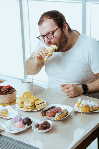 Man sitting in front of a table full of sweet food, eating pastry with cream. stock photo