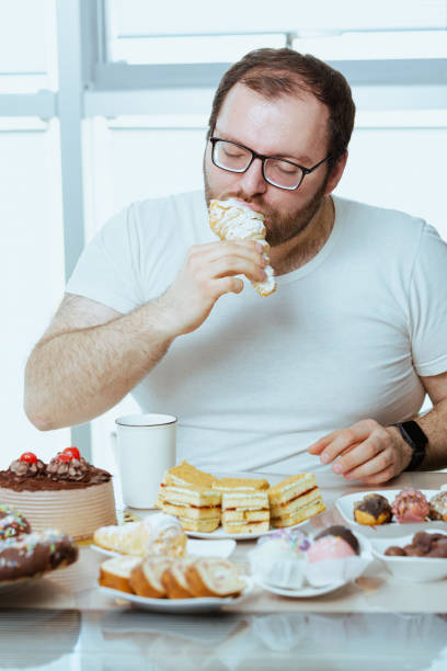 Man sitting in front of a table full of sweet food, eating pastry with cream. stock photo