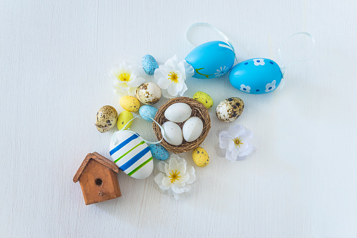 Easter eggs, birdnest with eggs and flowers on a white background; top view