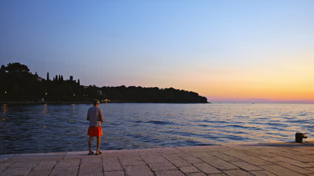 Man Fishing while Standing on Promenade in Front of Tranquil Sky at Dusk