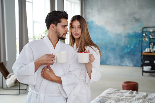 Free weekend, honeymoon, breakfast in morning at home or hotel, real love and relationship concept. Happy young couple with hot coffee in cozy bedroom interior.