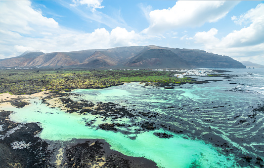 Discover the tranquil Caletón Blanco in Lanzarote, where volcanic rocks cradle turquoise waters against a backdrop of dramatic mountains.